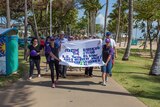A group of people wearing purple shirts walk along The Strand in Townsville