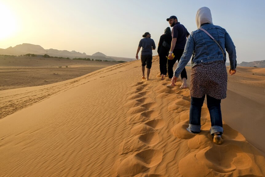 Men and women walk along a sandbank. 