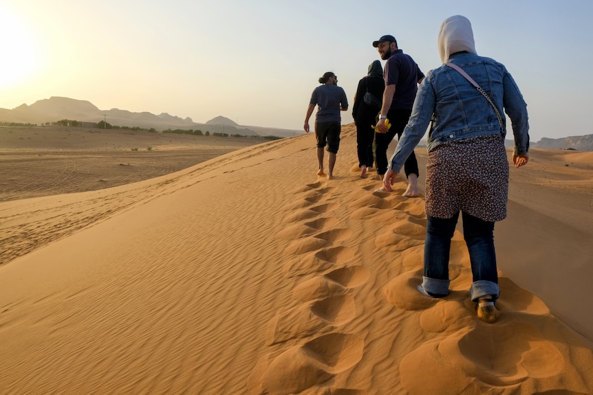 Men and women walk along a sandbank. 
