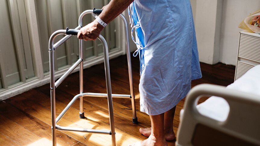 Old person in hospital gown using walker.