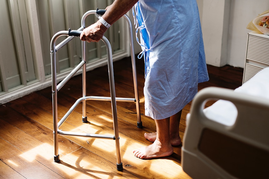 Old person in hospital gown using walker.