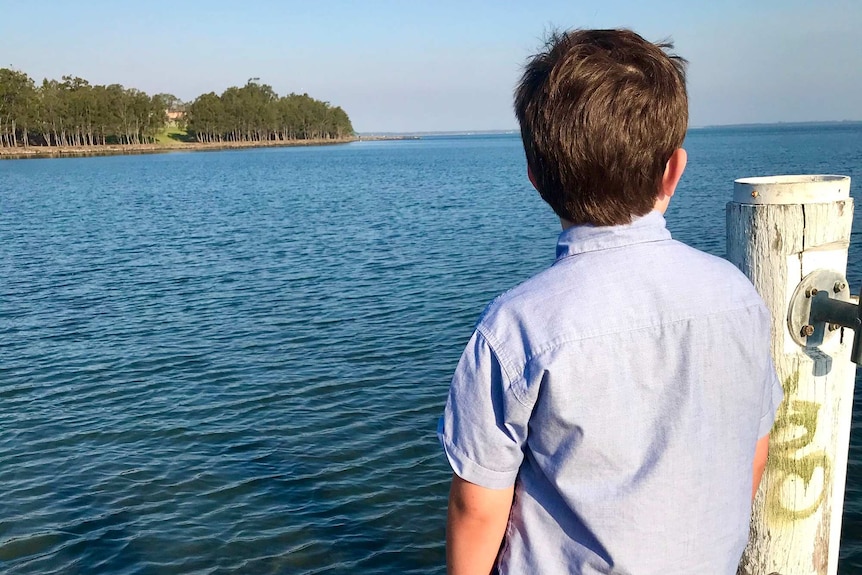 A boy stands looking out at the ocean with his back to the camera.