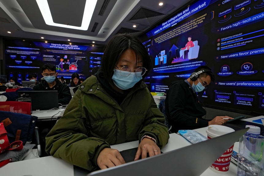 Trabajadores de tecnología chinos se sientan frente a computadoras rodeados de pantallas brillantes
