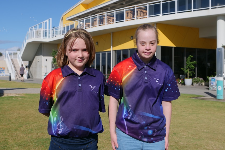 Two young people standing on the grass with a building behind them smiling at the camera