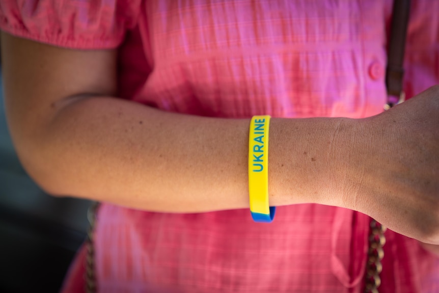 Womans arm with a yellow and blue arm band with 'ukraine' etched on it.