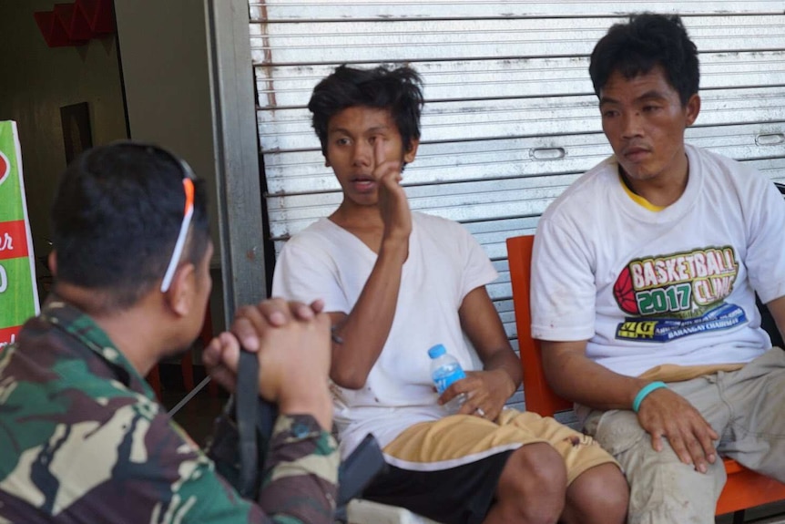 Three Christians wearing white shirts talk after fleeing Islamic State fighters in Marawi.