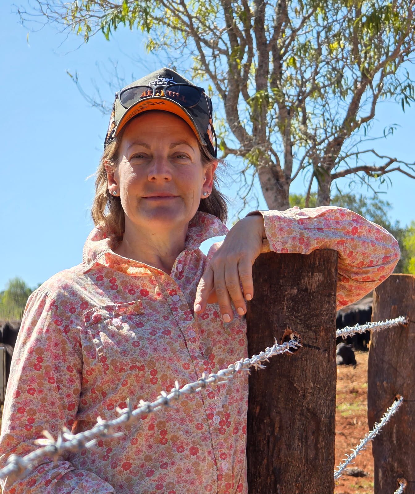 A woman in a cap leans against a barbed wire fence.