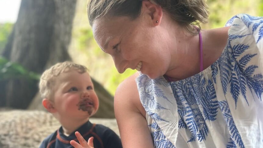A toddler smiles at his mum. His face is covered in chocolate ice cream