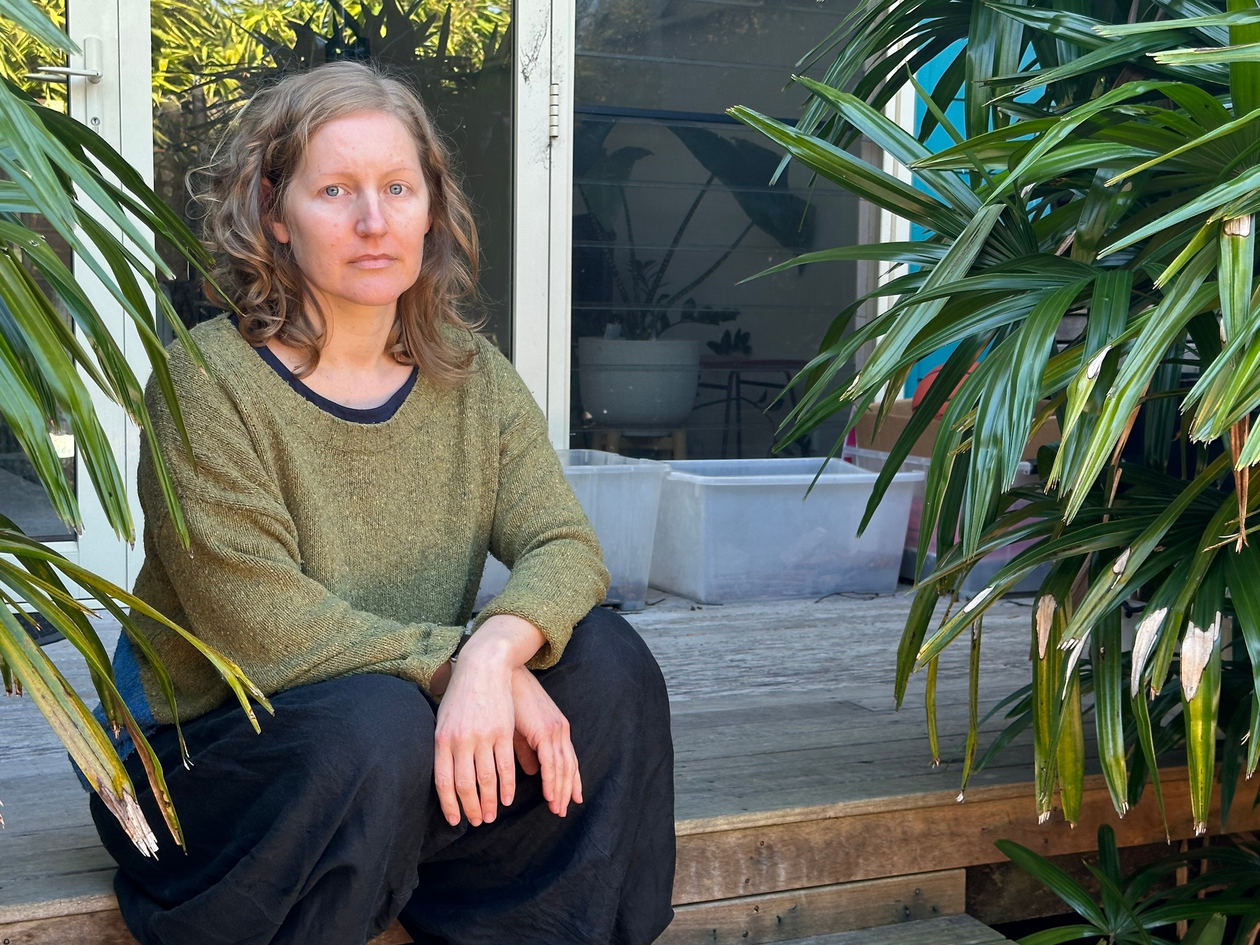 A white woman with brown hair sitting on a step outside a house