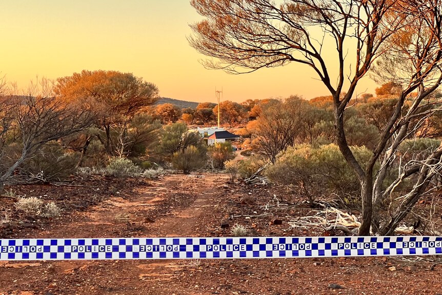 A wide shot of bushland with police tape in the foreground and a police tent in the distance between trees and bushes.