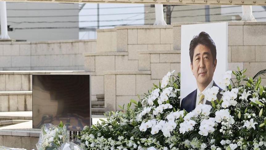 large image of Shinzo Abe on table surrounded by white flowers