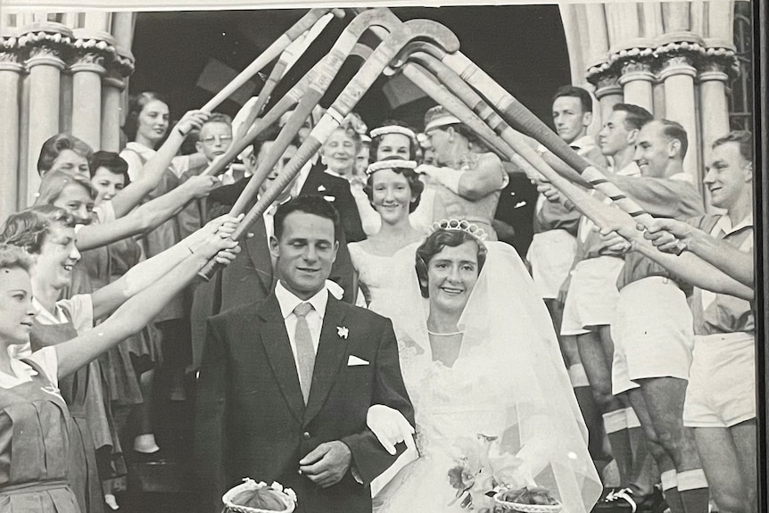 Daphne et Mick Pirie le jour de leur mariage alors que les hommes utilisent des bâtons de hockey pour les saluer.