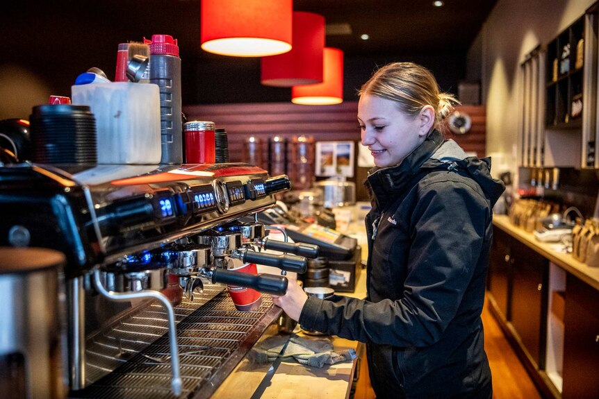 A woman makes a coffee behind a coffee machine inside a cafe.