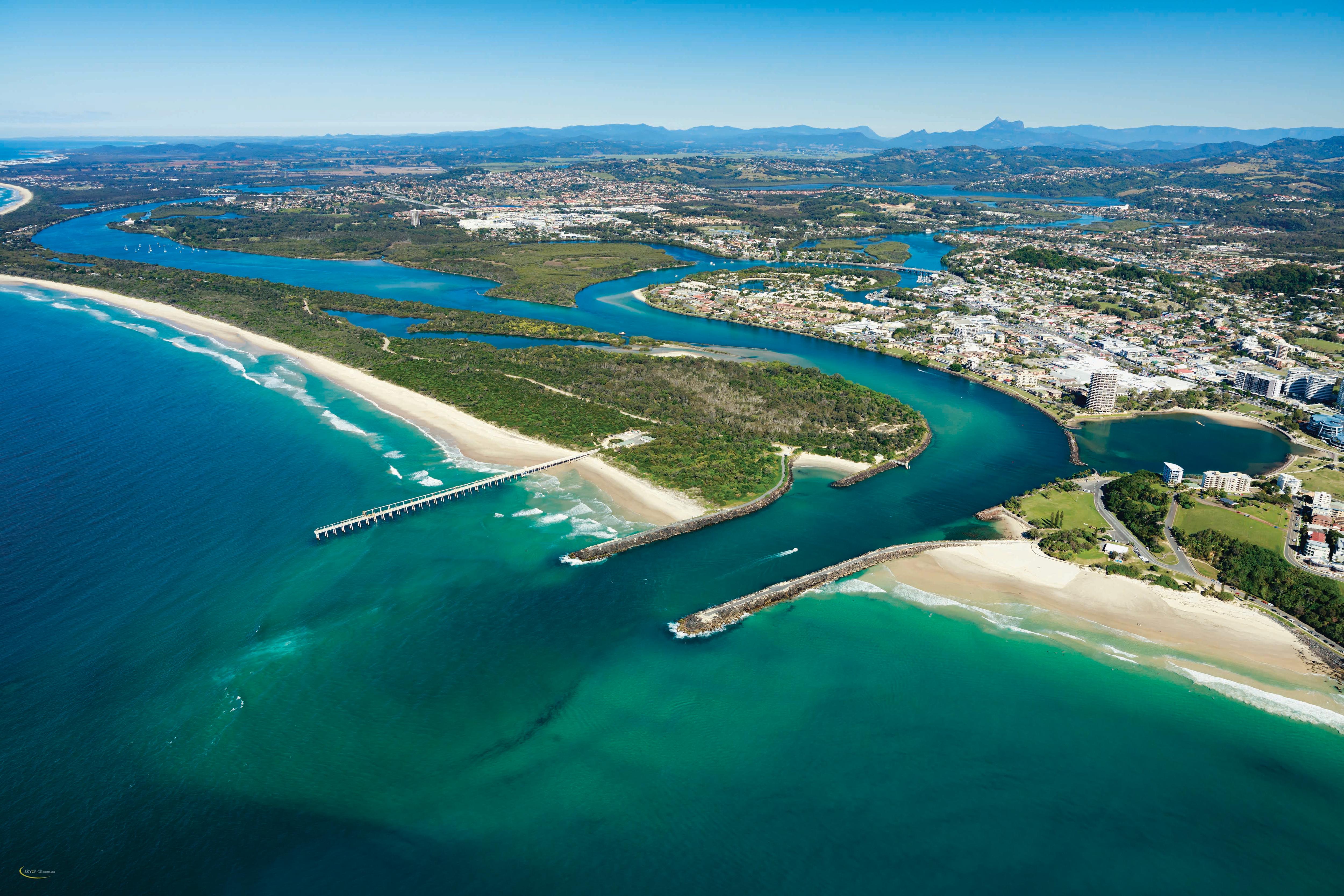 An aerial photo of a river mouth with an urban area nearby and a mountain range in the background.