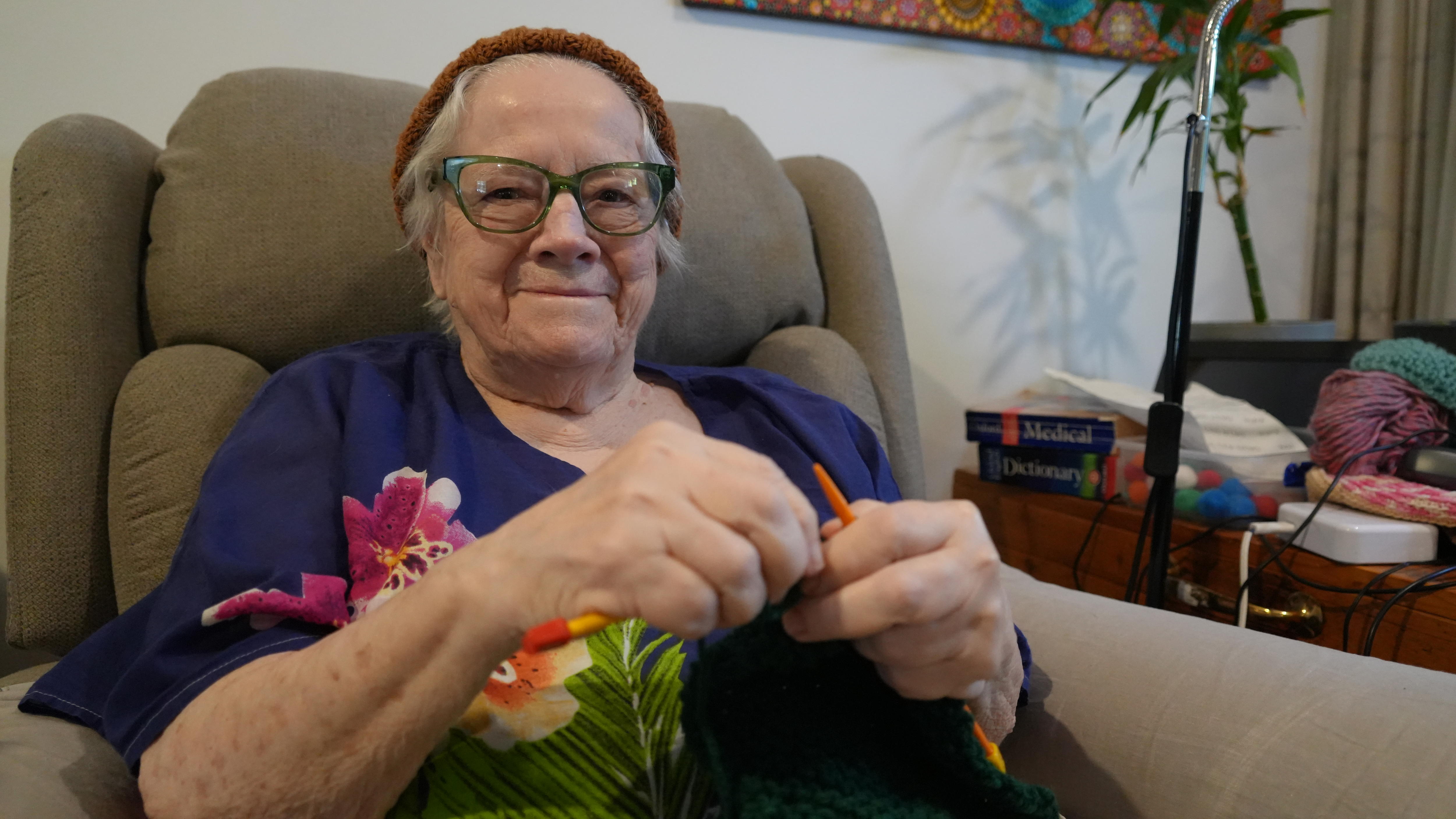 An older woman wearing a beanie as she knits yarn.