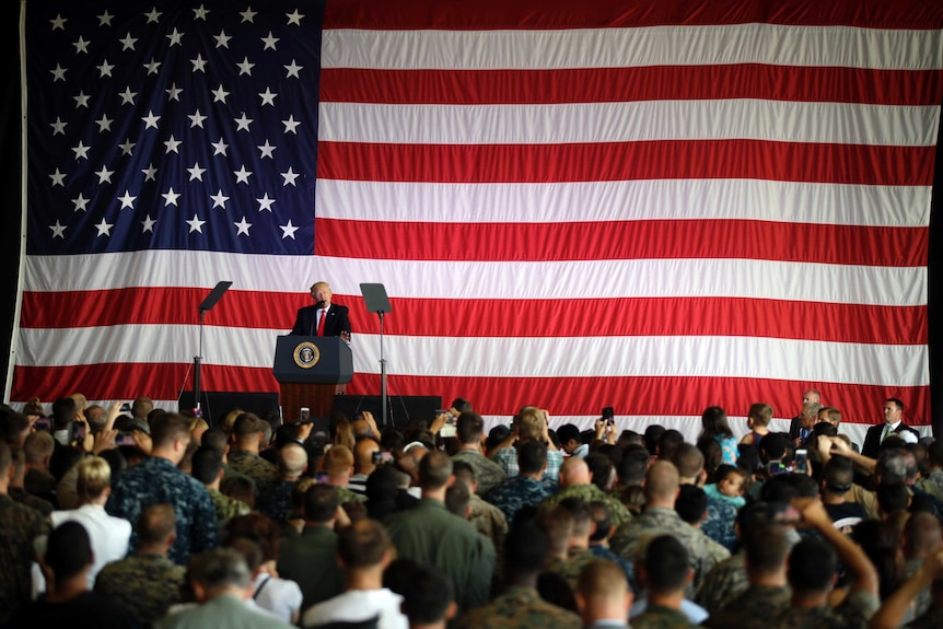 Donald Trump stands in front of a giant US flag, addresses US troops at a naval base.