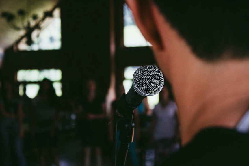 A person, out of focus, is speaking into a microphone to a group of people