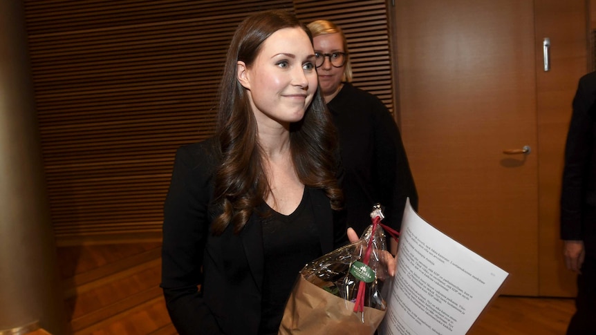 Finnish politician Sanna Marin looks off-camera and smiles, holding documents.