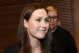 Finnish politician Sanna Marin looks off-camera and smiles, holding documents.