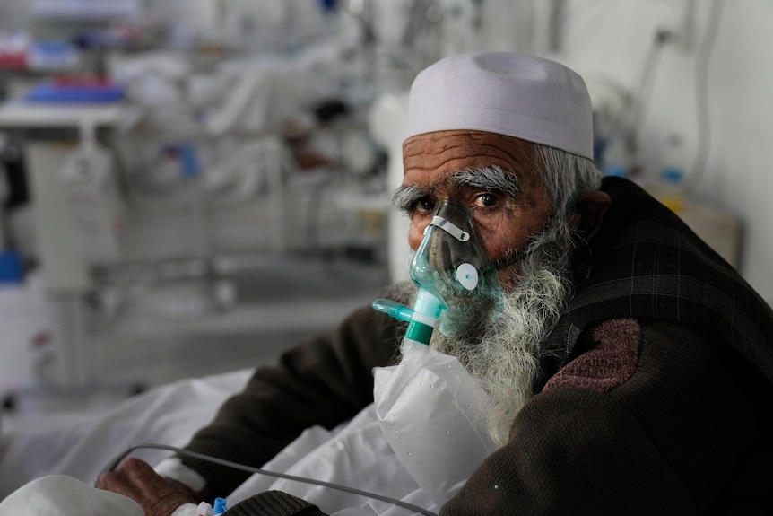 Elderly Afghan man wearing an oxygen mask sits in hospital. 