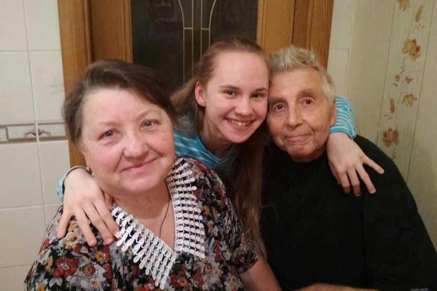 Young woman stands between elderly couple, smiling at the camera 