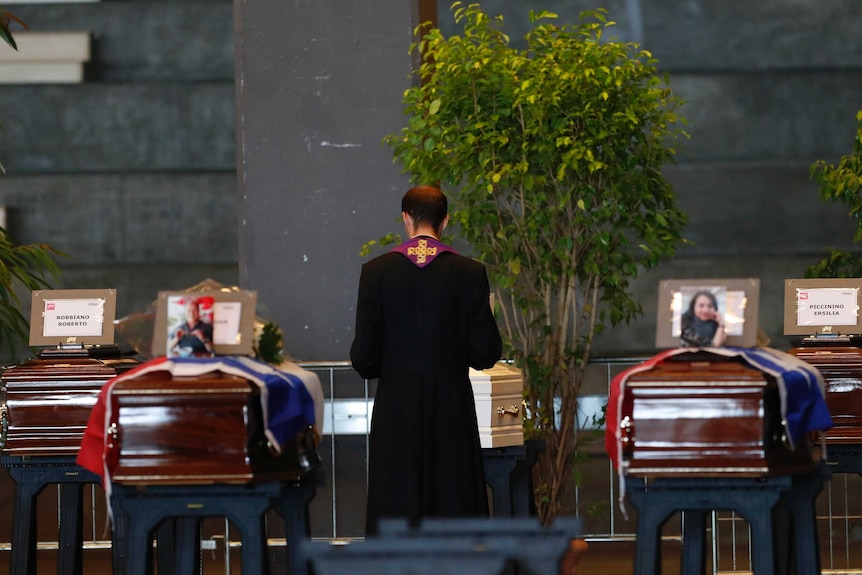 A priest stands by coffins of the victims at the Genova exhibition centre.