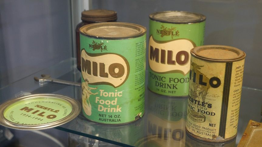 Three old green tins with retro font spelling Milo sit on shelf.