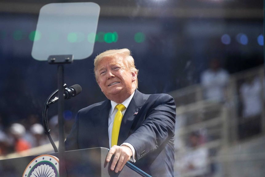 Donald Trump stands in front of a podium.