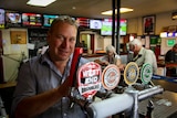 A white, blonde-haired man in a blue plaid shirt smiles and pours a beer at the Swan Reach Hotel bar.