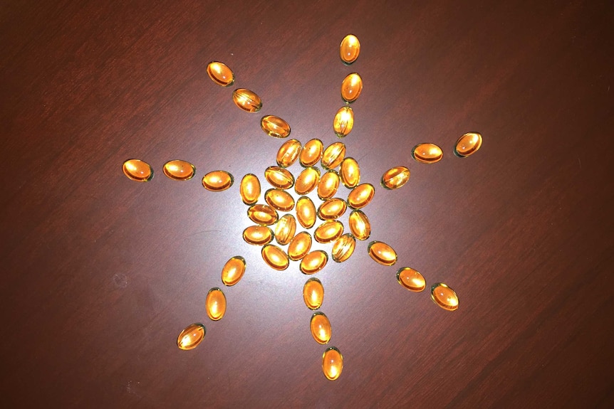 Golden-coloured capsules of vitamin D in the shape of a sun on a brown table