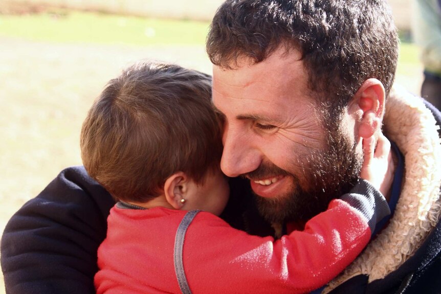 A man smiles as he holds a child in his arms.