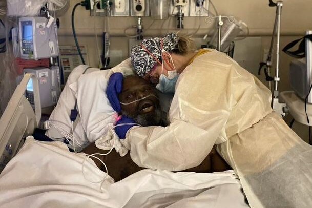 A woman hugs a man on a hospital bed.