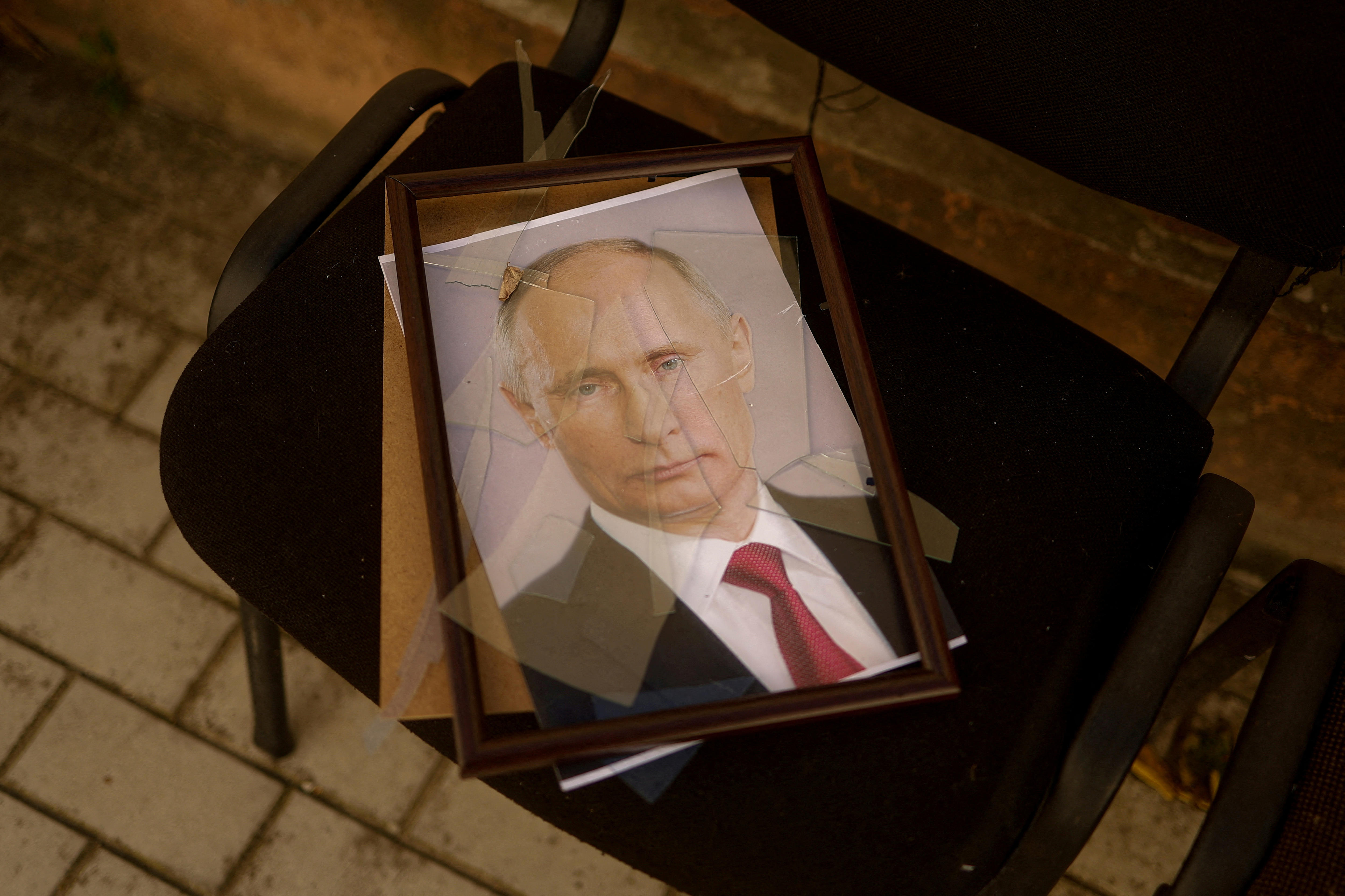 A framed photograph of Vladimir Putin sits on a chair, the glass smashed