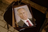 A framed photograph of Vladimir Putin sits on a chair, the glass smashed