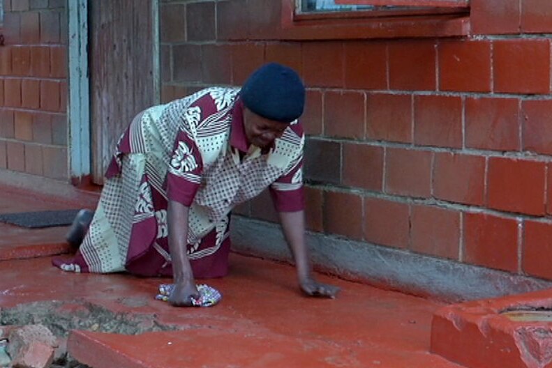 Margaret Chibanda crawls on all fours on the teracotta tiles outside her house