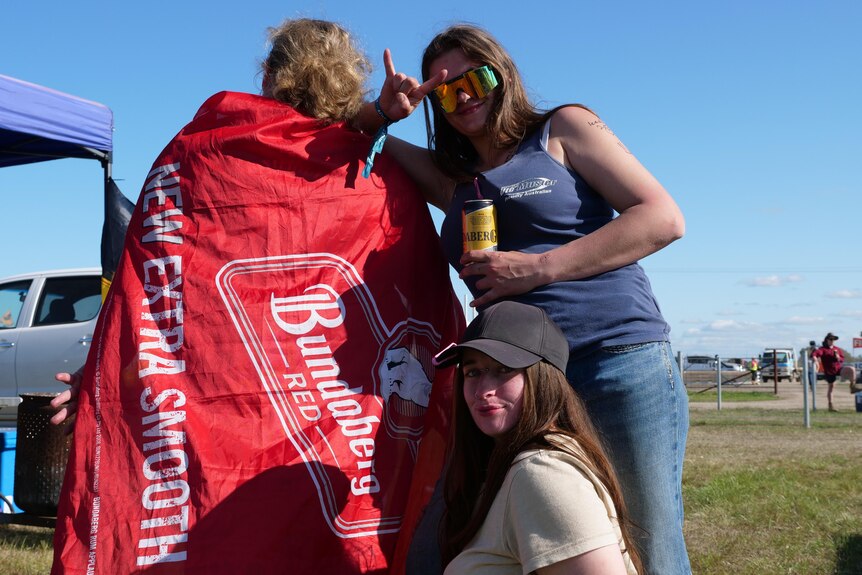 One woman draped in a Bundaberg Rum flag and two friends pose for the camera.