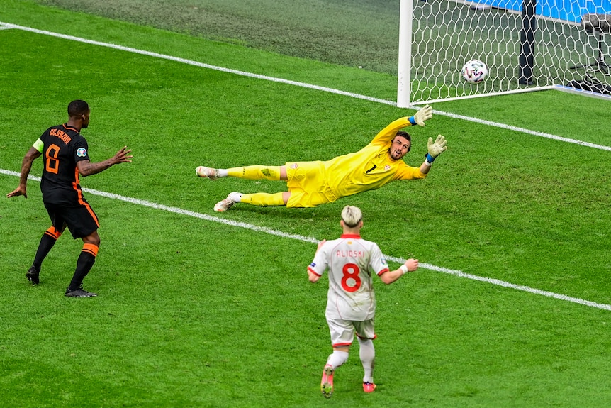 A Dutch player stands and watches his shot hit the net as the grounded goalkeeper raises his arms during a Euro 2020 match.