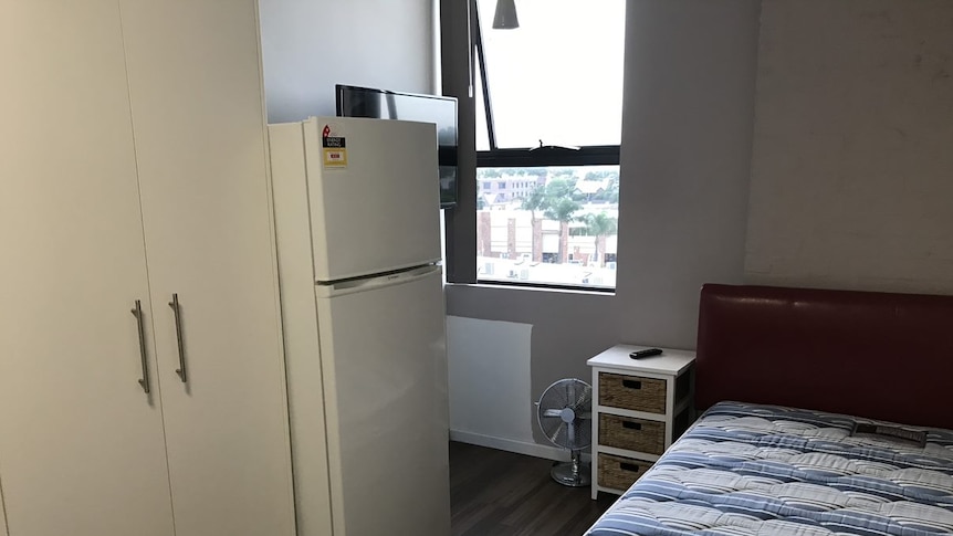 A fridge, cupboard and bed inside a mico apartment in Sydney