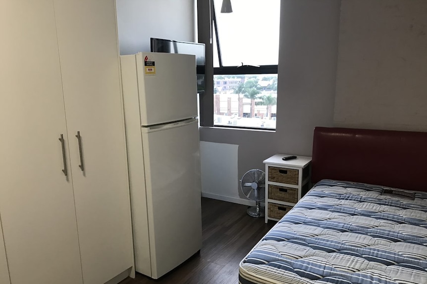 A fridge, cupboard and bed inside a mico apartment in Sydney