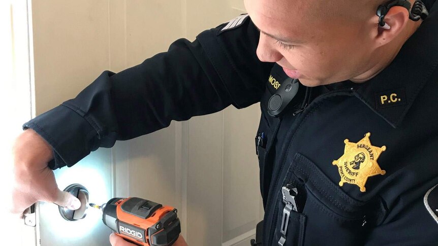 A police officer drilling a lock into a door