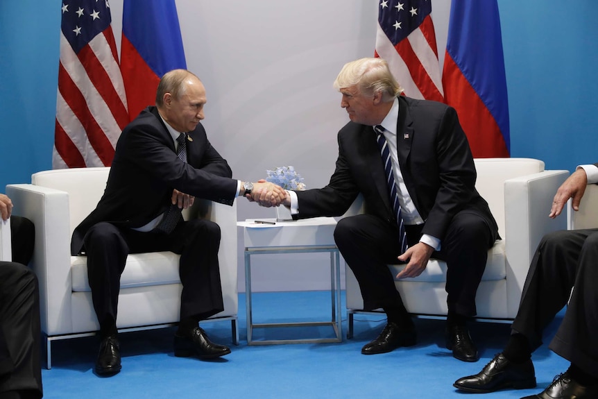 Donald Trump and Vladimir Putin look at each other and smile while shaking hands at the G20 Summit.