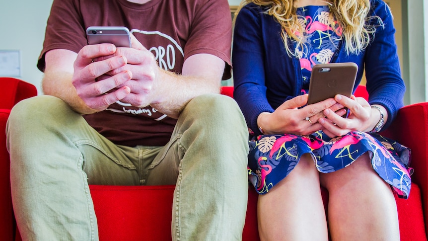 A couple sits looking at their phones.