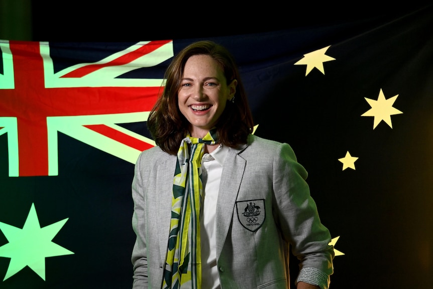 Cate Campbell smiles and stands in front of an Olympic flag.