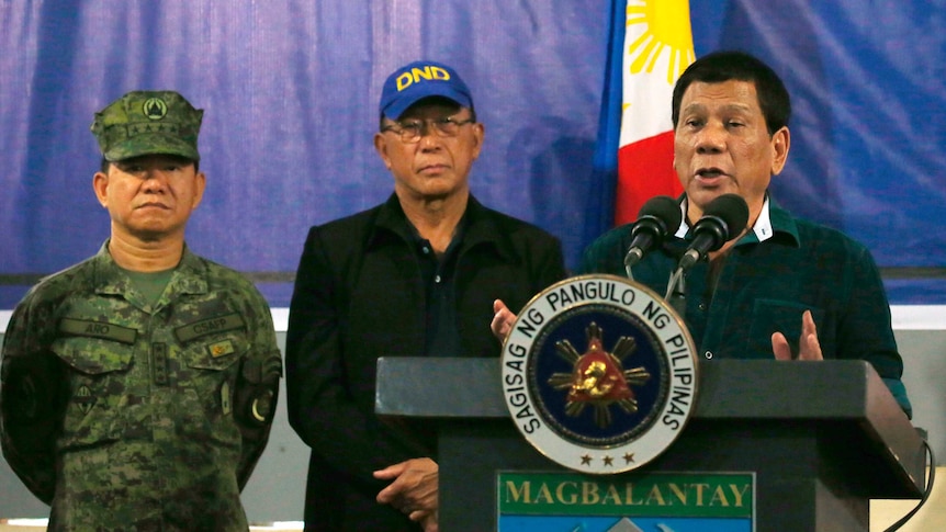 Philippine President Rodrigo Duterte speaks at a lectern, flanked by military personnel.