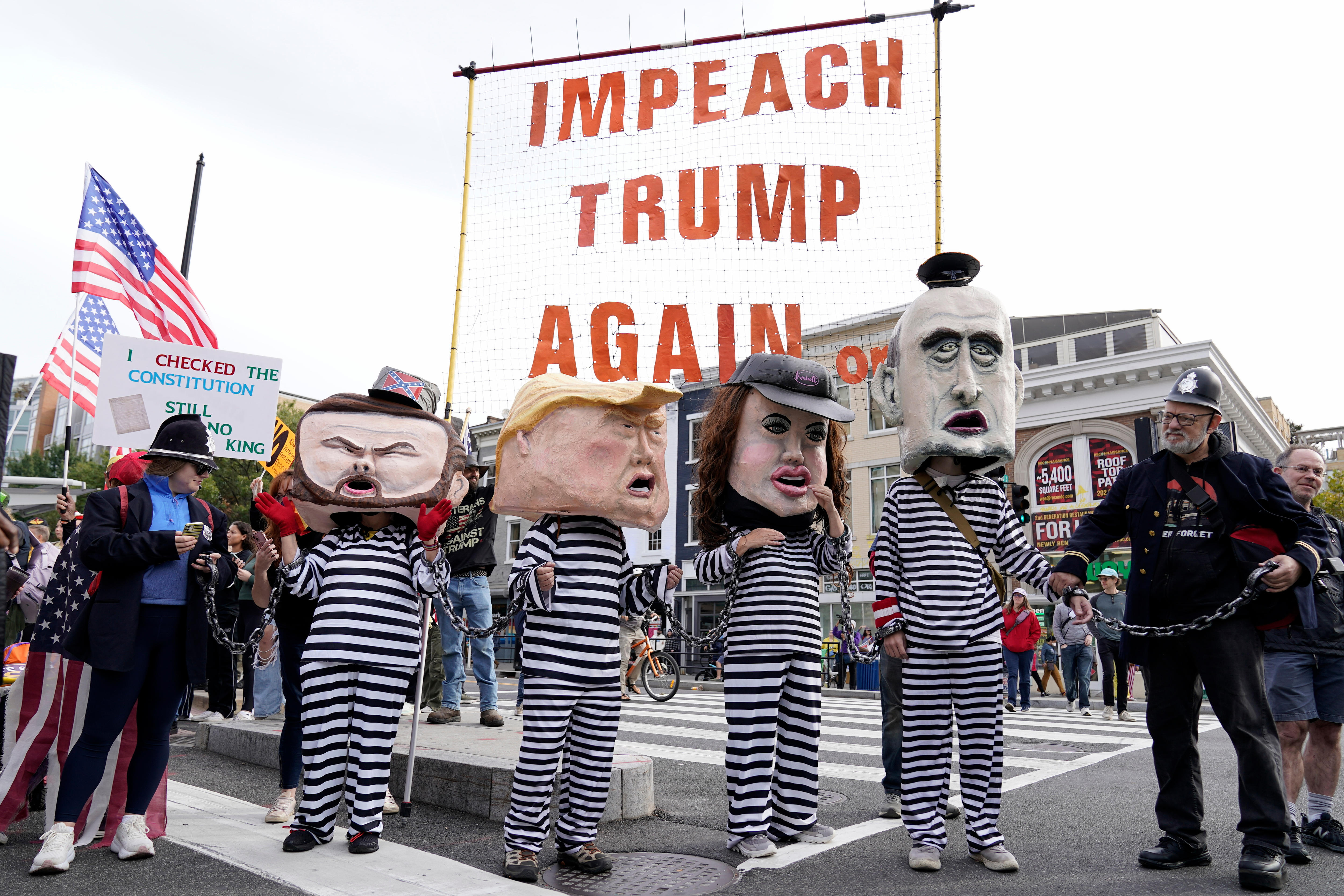Protesters in fake Donald Trump and prisoner costumes standing next to an 'Impeach Trump Again' sign