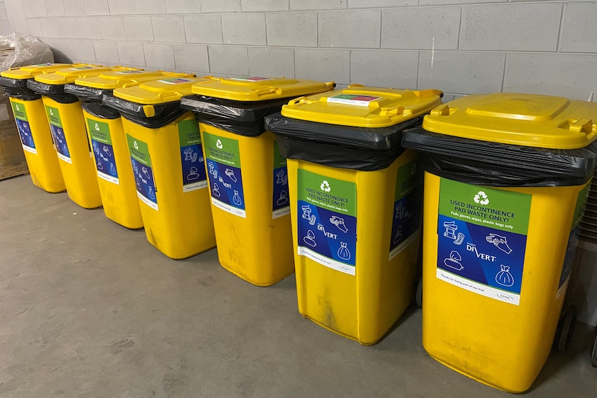 A row of yellow waste bins at Wilson Lodge in Sale. The bins are marked: used incontinence pad waste only.