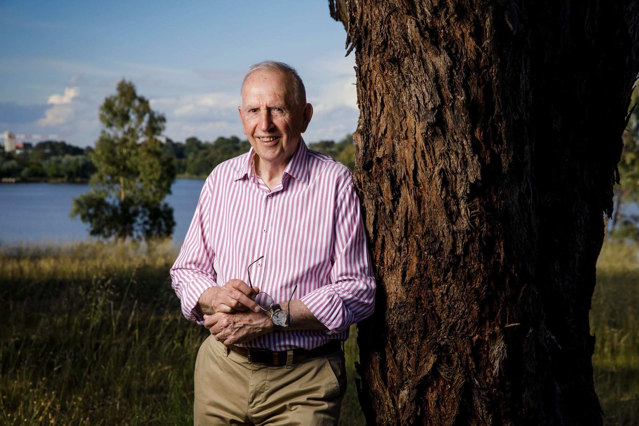 An elderly man leaning against a tree and smiling.
