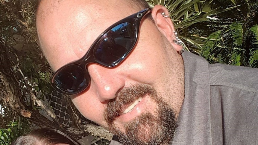 A smiling man with a beard wearing dark sunglasses