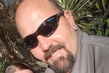 A smiling man with a beard wearing dark sunglasses