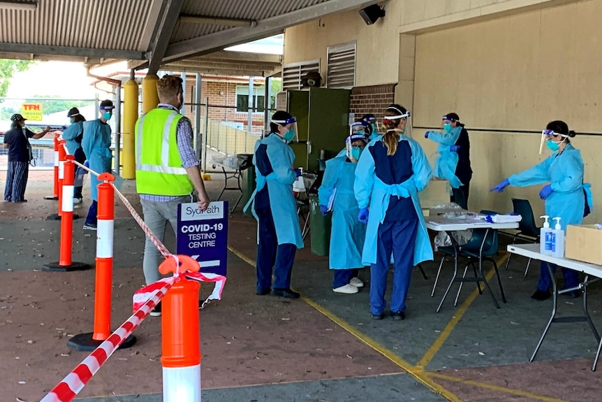 People wearing face masks and shields and blue medical aprons set up a COVID-19 testing clinic at a school.